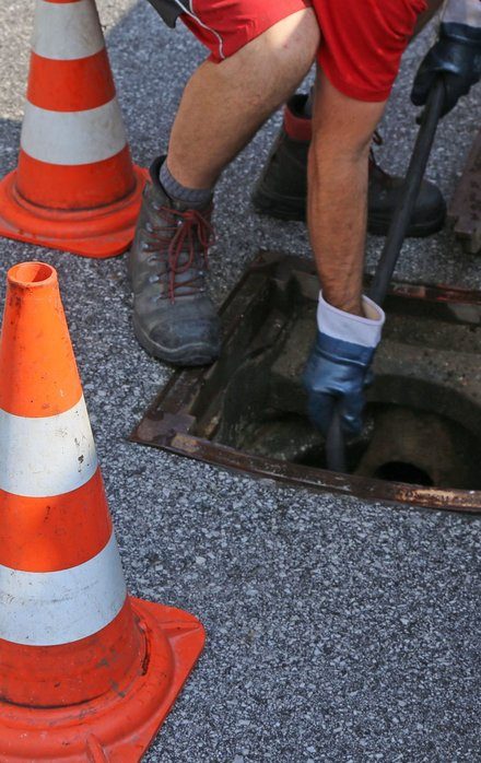 Drainage engineer at a manhole with safety cones